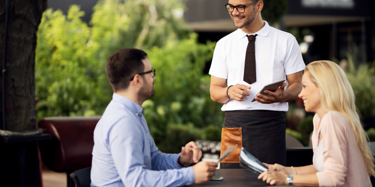 young smiling waiter talking to a couple while taking their order in a cafe.